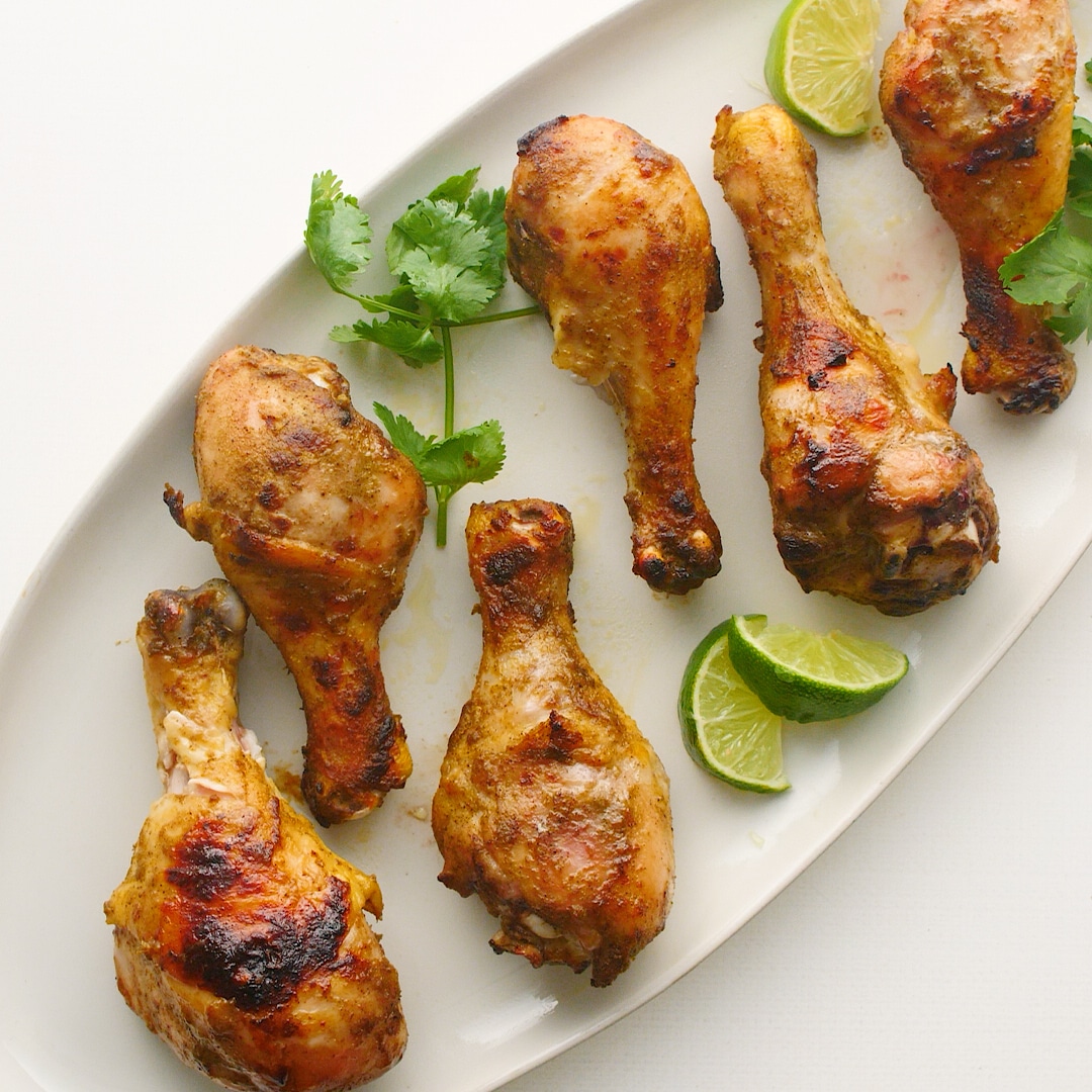 6 Jamaican jerk chicken drumsticks with lime slices on a white plate