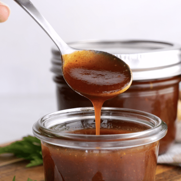 A spoonful of homemade barbecue sauce dripping into a jar of the same.