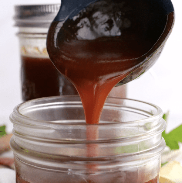 Pouring homemade BBQ sauce into a large mason jar.