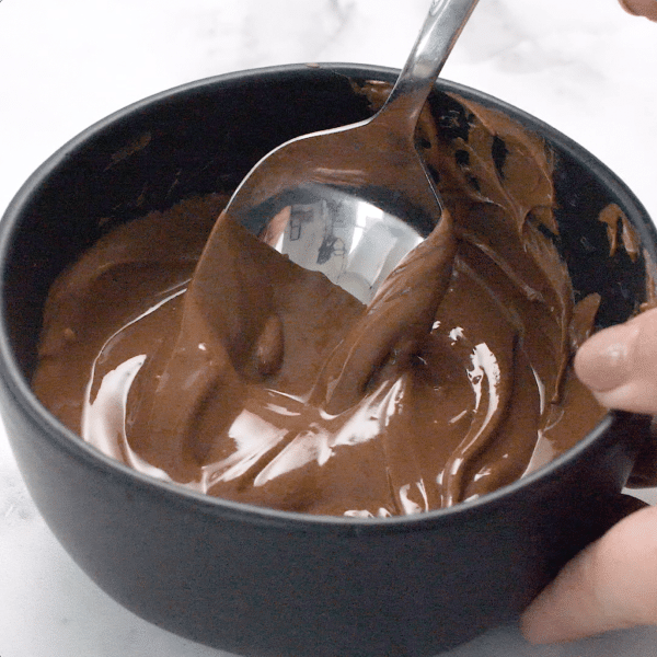 Spoon stirring melted chocolate in a bowl held by a hand.