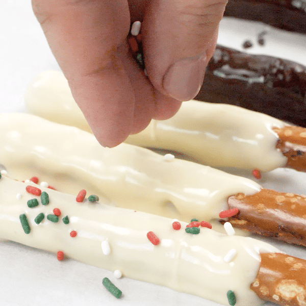 Hand topping white chocolate covered pretzels with sprinkles.