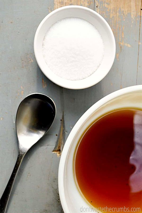 A bowl of herbal water soaks in a white bowl. A metal spoon rests next to the bowl.