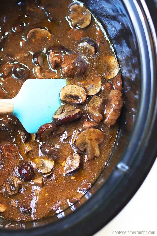 Beef stroganoff in a slow cooker with a silicone spoon stirring.