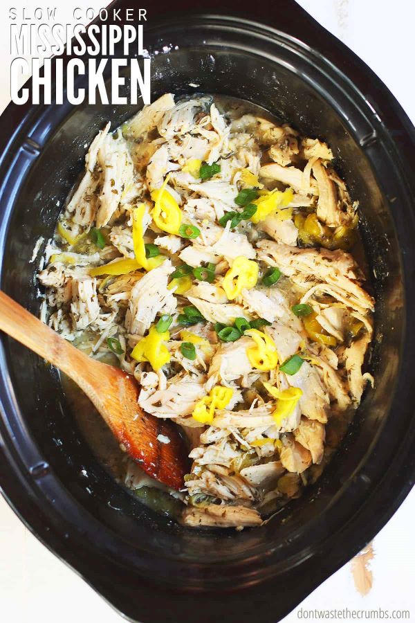 Crock Pot Mississippi Chicken recipe freshly cooked in a black oval slow cooker with chicken breast, seasonings, pepperoncini, and finished with green onions. The text overlay reads 'Slow Cooker Mississippi Chicken.'