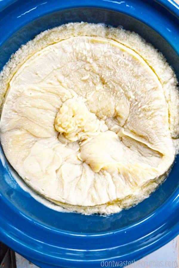 Neutralized soap, its texture thick and lightened to the color of bread dough, rests in a crock pot.