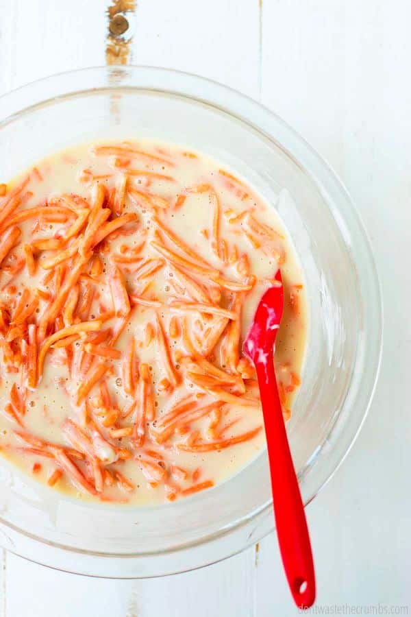 Large glass bowl with liquid and shredded carrots and  red spoon.