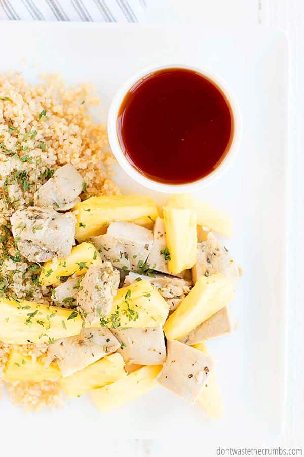 Pineapple chicken over quinoa with a small white bowl of fresh sweet and sour sauce.