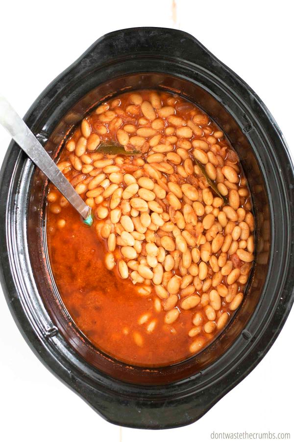 Baked beans in a slow cooker with a ladle in it.