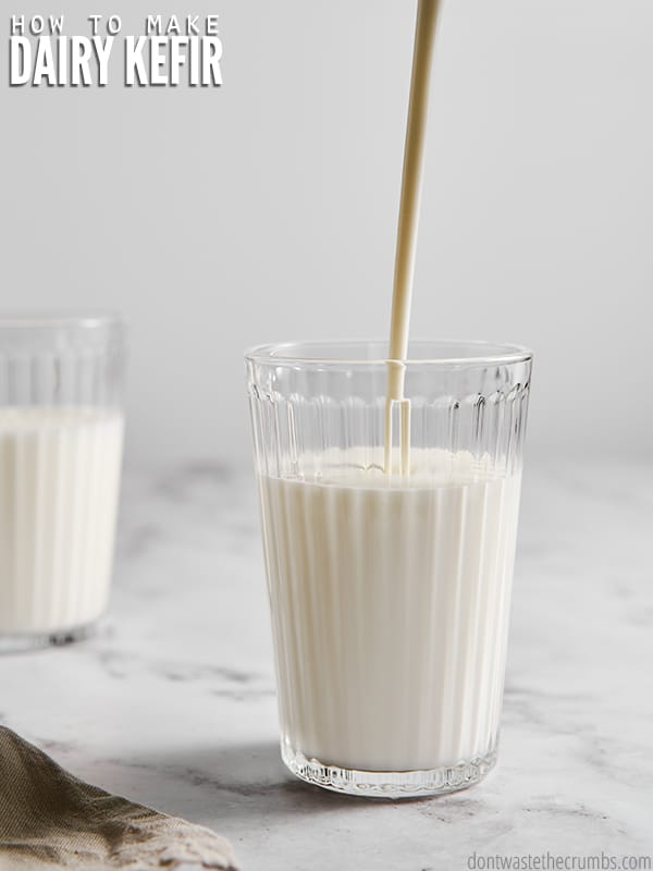 Glass cup of homemade kefir with liquid pouring into it. Text overlay reads, "How To Make Dairy Kefir".