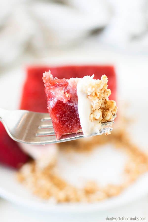 A big delicious bite of pretzel salad with strawberries on a fork.