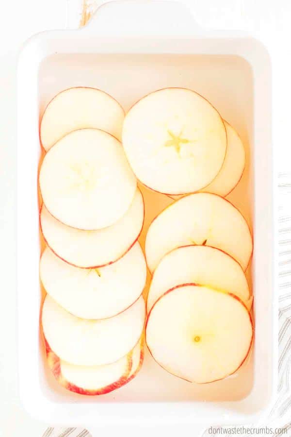 Sliced apples resting in a white bowl filled with water, lemon juice, and cinnamon.