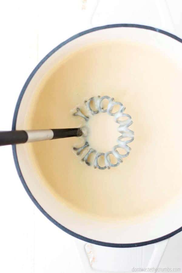 Cheese sauce being stirred with a whisk to help incorporate the milk, flour, butter and cheese. 