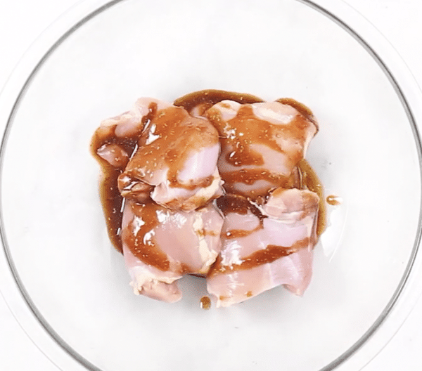 Raw chicken with a sauce drizzled all over in a glass mixing bowl.