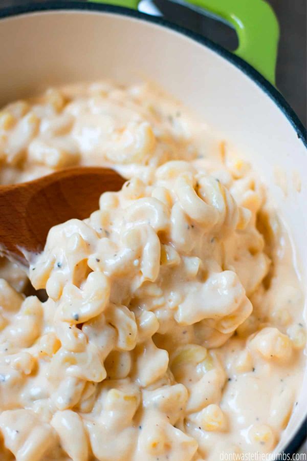 Freshly made macaroni and cheese in a green Dutch oven being served with a wooden spoon. 