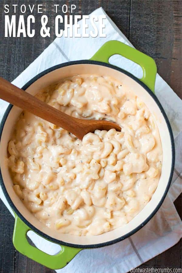 A green Dutch oven pot with freshly made mac and cheese, stirred with a wooden spoon. The text overlay reads, "Stove Top Mac & Cheese."