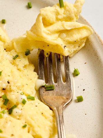 Cottage cheese and eggs garnished with chives on a plate with a bite ready to eat on a fork.